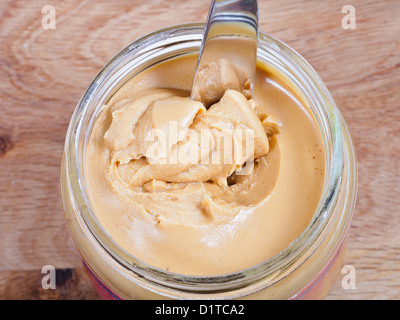 Erdnussbutter mit Messer in einem Glas auf Holztisch Stockfoto