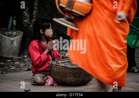 LUANG PRABANG, Laos – buddhistische Mönche und Novizen in hellen Safrangewändern spazieren in einer einzigen Datei durch die Straßen von Luang Prabang während der frühen Morgenzeremonie, bekannt als Tak Fledermaus. Einheimische und Touristen säumen die Strecke und bieten Speisen in diesem täglichen Ritual an, das im Zentrum der buddhistischen Tradition Laos steht. Stockfoto