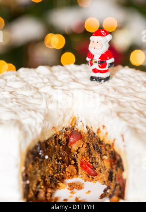 Schneiden Sie aus vereisten Weihnachtskuchen mit Lichter der Weihnachtsbaum im Hintergrund unscharf Stockfoto