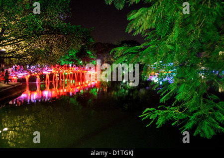 HANOI, Vietnam – die Huc-Brücke (Morgensonnenbrücke) mit Bäumen bei Nacht. Die rot gestrichene Holzbrücke verbindet das Nordufer des Sees mit der Jade Island und dem Tempel des Jade Mountain (Ngoc Son Temple). Stockfoto