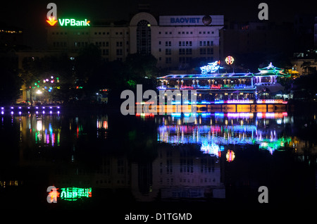 HANOI, Vietnam – Stadtlichter von Gebäuden entlang der nordwestlichen Küste des Hoan Kiem Lake erzeugen Reflexionen auf der ruhigen Wasseroberfläche. Der historische See in der Altstadt von Hanoi ist ein zentrales Merkmal der nächtlichen Landschaft der Stadt. Die Uferpromenade verbindet Architektur aus der Kolonialzeit mit moderner Beleuchtung. Stockfoto