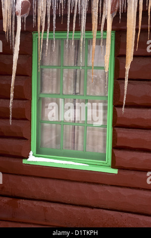 Nahaufnahme von einem Blockhaus-Fenster mit Eiszapfen hängen von der Decke über dem Fenster Stockfoto