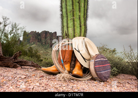 Ein Cowboy Cowboys Stiefel, Hut, Lasso und Kantine Rest gegen ein Kaktus in extremen, robuste Wüstengebiet. Stockfoto