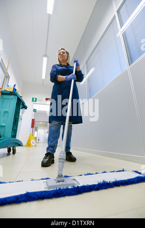 Frau arbeitet, professionelle Magd Bodenreinigung mit Besen in Industriegebäude. Voller Länge, niedrigen Winkel Ansicht Stockfoto