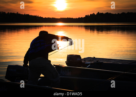 Silhouette der Fischer, die den Motor seines Bootes mit gelb und orange Sonne im Hintergrund beginnt Stockfoto