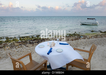 Tisch im Restaurant am Strand bei Sonnenuntergang über der Karibik, East End von Grand Cayman. Stockfoto