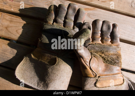 Verschlissene Arbeitshandschuhe auf Holzbank, starke Schatten Stockfoto