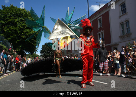 Karnevalsumzug Darsteller in einer sonnendurchfluteten Straße. Ein Mann in einem roten Hut und Anzug schaut in Richtung Kamera. Stockfoto