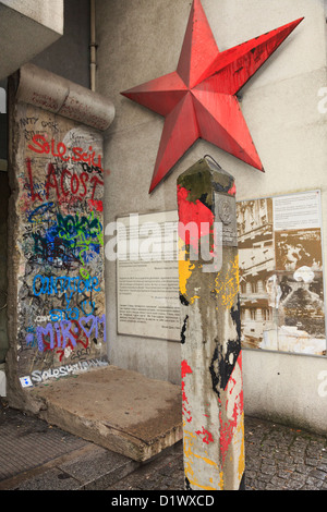 Graffiti auf einem Abschnitt der Mauer mit Informationen, roter Stern und eine original DDR-Grenze post außerhalb Checkpoint Charlie Museum Stockfoto