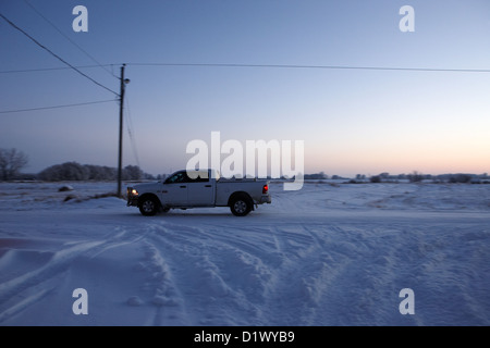 LKW-fahren durch die untergehende Sonne über ländliche schneebedeckten Szene in abgelegenen Dorf vergessen Saskatchewan Kanada Stockfoto