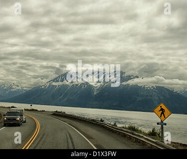 29. Juni 2012 übersät - Halbinsel Kenai, Alaska, USA - A Bullet Fußgängerüberweg Zeichen [Rght] Süden entlang malerischen Seward Highway fahren. Es Röcke die Basis der Chugach Mountains und bietet spektakuläre Ausblicke auf die vergletscherten, schneebedeckten Kenai Mountains eingerahmt von dramatischen Wolkenformationen. Sie ragen in der Ferne Turnagain Arm, bei Ebbe das Wasser nur über die Bucht. Bezeichnet einen National Forest Scenic Byway, ein All-American Road und eine Alaska Scenic Byway, läuft Seward Highway 127 Meilen [204 km] von Anchorage, Seward auf der Kenai-Halbinsel, Chugach State Park und Stockfoto