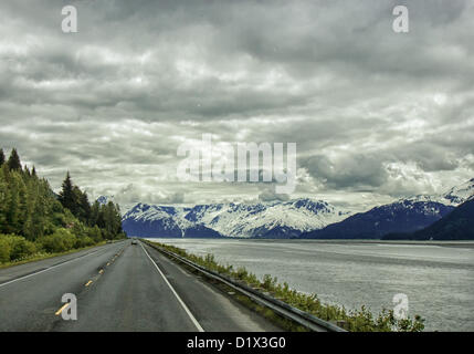 29. Juni 2012 - Halbinsel Kenai, Alaska, USA - Süd, malerische Seward Highway fahren Röcke die Basis der Chugach Mountains [Links] und bietet spektakuläre Ausblicke auf die vergletscherten, schneebedeckten Kenai Mountains eingerahmt von dramatischen Wolkenformationen. Sie steigen in der Ferne über Turnagain Arm--bei Ebbe das Wasser nur über die Bucht. Bezeichnet einen National Forest Scenic Byway, ein All-American Road und eine Alaska Scenic Byway, läuft Seward Highway 127 Meilen [204 km] von Anchorage, Seward, Kenai-Halbinsel, Chugach State Park und Chugach National Forest, ein Schaufenster der natürlichen beau Stockfoto