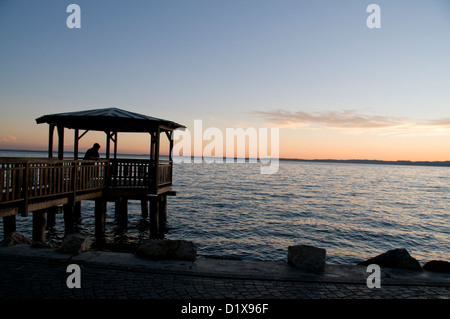 Der Sonnenuntergang über der halbkreisförmigen Bucht in der Stadt Garda am Ostufer des Gardasees in der Region Vento in Norditalien. Stockfoto