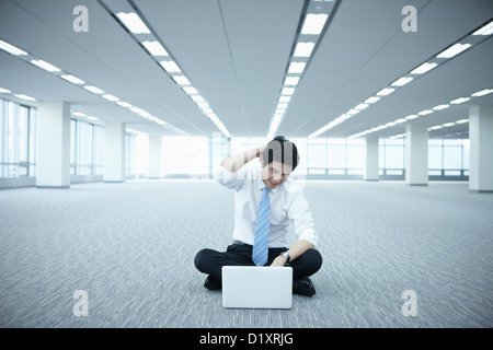 Ein gestresster Geschäftsmann mit Laptop auf dem Boden von einem leeren Raum Stockfoto