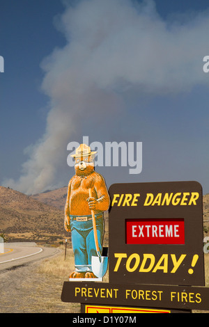 Smokey Bear extreme Feuer Warnschild mit einer Wolke aus Rauch von einem Waldbrand im Hintergrund in Boise County, Idaho, USA. Stockfoto