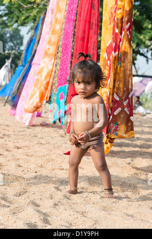 Indische Mädchen spielen im Sand neben Saris auf der Wäscheleine. Andhra Pradesh, Indien Stockfoto