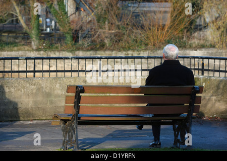 Ein älterer Mann sitzt auf seinen eigenen auf einem Park Bank mit Blick auf den Fluss Avon in Bath, Somerset, UK. Stockfoto