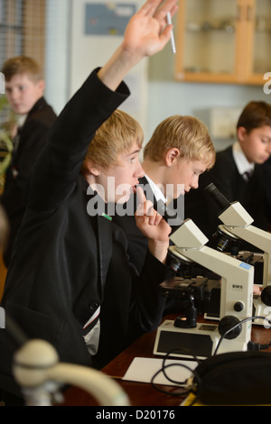 Schuljunge stellt eine Frage während der Verwendung eines Mikroskops während einer Unterrichtsstunde Wissenschaft an Pasteten Grammar School in Cheltenham, Barnwall Stockfoto