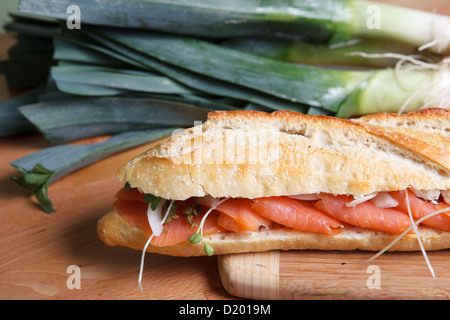 Frisch geräucherter Lachs Sandwich auf Baguette, auf Schneidebrett mit großen grünen Zwiebeln im Hintergrund Stockfoto