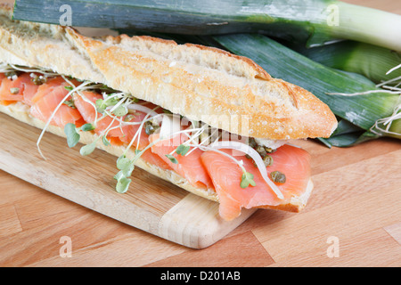 Frisch geräucherter Lachs Sandwich auf Baguette, auf Schneidebrett mit großen grünen Zwiebeln im Hintergrund Stockfoto