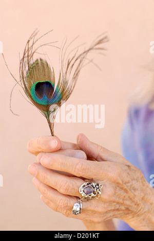 Die geschmückten Hand einer Frau in ihren 80 ist einer Pfauenfeder. Stockfoto