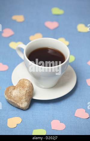 Eine Teetasse mit Tee steht auf der blauen Tischdecke mit Kuchen alle dekoriert mit Papierherzen Stockfoto