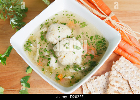 Eine einzige Portion von Koscher Matza Ball Suppe auf einem Holztisch, garniert mit frischen Karotten und Matzo Cracker Stockfoto