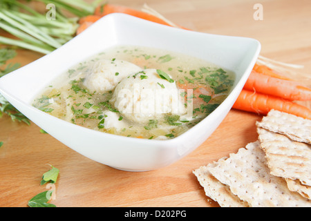 Eine einzige Portion von Koscher Matza Ball Suppe auf einem Holztisch, garniert mit frischen Karotten und Matzo Cracker Stockfoto