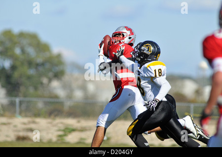 Fußball-Empfänger macht einen Durchgang Rezeption über die ausgestreckte Hand eines Defensive zurück bei einem High School Spiel. USA. Stockfoto