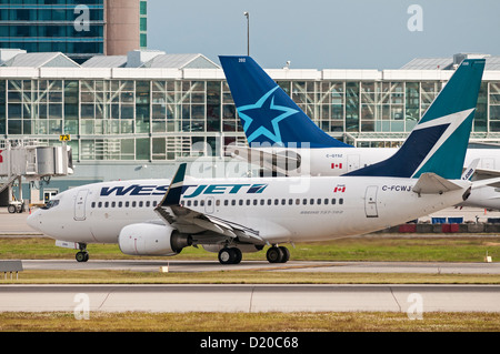 Ein Düsenflugzeug Westjet Boeing 737 rollt durch ein Jetliner Air Transat Airbus A330 auf dem Rollfeld in Vancouver International Airport Stockfoto