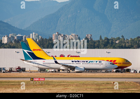 WestJet Boeing 737 air (737-800) Passagier Jetliner Taxis vorbei an einer DHL Boeing 767 Cargo Freighter (betrieben von ABX Air) Stockfoto