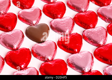 Schokoladenherzen in rot und Pick-Folie-Wrapper auf einem weißen Hintergrund mit einem ausgepackten Herzen in der Gruppe. Stockfoto