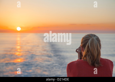 Junge Frau, die den Sonnenuntergang vom Kreuzfahrtschiff MS Deutschland (Reederei Peter Deilmann), Karibik, nahe Caym zu fotografieren Stockfoto
