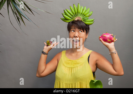 Glückliche Frau lächelnd mit frischem Obst in Händen und Bananen auf Kopf Stockfoto