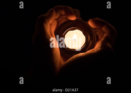 Hände in der Form eines Herzens um eine brennende Kerze. Stockfoto