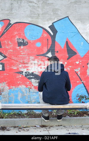 Junger Mann von der Rückseite mit Blick auf eine Graffitiwand bedeckt gesehen Stockfoto