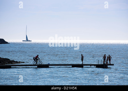 Silhouette von Segelschiff am Horizont, Fahrrad und Menschen auf einem Pier, Visby, Gotland, Schweden, Europa Stockfoto