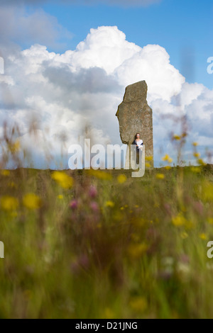 Junge Frau steht von Stein bei The Ring of Brodgar Kreis der neolithischen Menhire, Orkney Islands, Schottland, Vereinigtes Königreich Stockfoto
