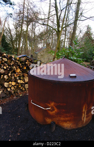 Ein traditioneller Holzkohlebrenner Ofen oder Ofen und ein Stapel Von Baumstämmen in einer Waldlichtung in Nordwales für Herstellung von traditionellen Holzkohle Brennstoff Stockfoto