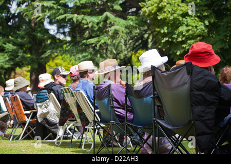 Eine Reihe von Menschen sitzen, tragen Hüte, Unterhaltung zu beobachten. Hagley Park, Christchurch, Canterbury, Südinsel, Neuseeland. Stockfoto