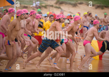 Sydney, Australien. 13. Januar 2013. Das Avalon Beach 1,5km Ocean Swim Race, Teil der pittwater Ocean Swim Reihe von Veranstaltungen, Avalon Beach, Sydney, Männer Race beginnt und männliche Wettkämpfer in pinken Schwimmkappen laufen am Strand in Richtung Meer Stockfoto