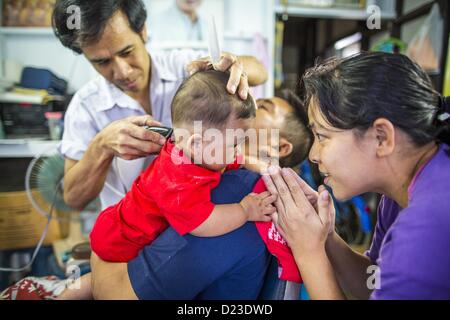 13. Januar 2013 tröstet - Bangkok, Thailand - eine Frau ihren Sohn, während er seinen ersten Haarschnitt im Stadtteil Bang Luang in Bangkok bekommt. Stadtteil Bang Luang Linien Khlong (Kanal) Bang Luang in der Thonburi-Sektion von Bangkok auf der westlichen Seite des Chao Phraya Flusses. Es wurde Ende des 18. Jahrhunderts von König Taksin dem großen gegründet, nachdem die Birmanen die siamesische Hauptstadt Ayutthaya entlassen. Die Nachbarschaft, wie die meisten von Thonburi, ist relativ unerschlossen und noch Kreuz und quer durchzogen von den Kanälen, die einmal Bangkok berühmt gemacht. Es ist nun ein beliebter Tagesausflug vom Zentrum von Bangkok und bietet einem gli Stockfoto