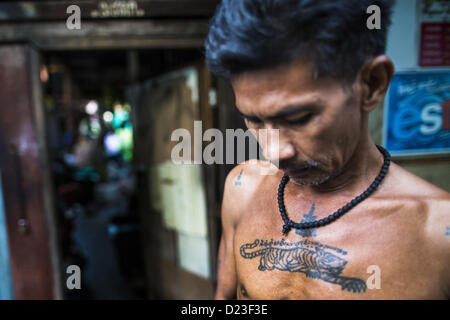 13. Januar 2013 - Bangkok, Thailand - ein Mann mit einem '' Sak Yant'' oder Heilige Tiger Tattoo auf der Brust vor seinem Haus im Stadtteil Bang Luang von Bangkok. Er glaubt, dass das Tattoo ermöglicht ihm, die Kraft des Tigers zu kanalisieren. Stadtteil Bang Luang Linien Khlong (Kanal) Bang Luang in der Thonburi-Sektion von Bangkok auf der westlichen Seite des Chao Phraya Flusses. Es wurde Ende des 18. Jahrhunderts von König Taksin dem großen gegründet, nachdem die Birmanen die siamesische Hauptstadt Ayutthaya entlassen. Die Nachbarschaft, wie die meisten von Thonburi, ist relativ unerschlossen und noch Kreuz und quer durchzogen von den Kanälen, Stockfoto