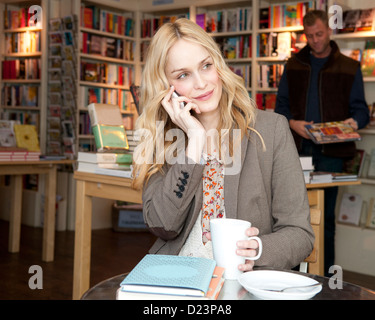 Eine Frau in einer Buchhandlung, Kaffee trinken und telefonieren mit ihrem Handy Stockfoto