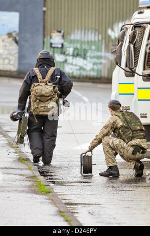 Belfast, Nordirland, Großbritannien. 14. Januar 2013. Armee ATO von 321 Squadron, 11 EOD Regiment, in eine Bombe gekleidet - Beweis für Spaziergänge in Richtung eines Verdächtigen gerät Durchführung elektronischer Zähler messen (L) und einer kontrollierten Explosion 'Pig' (R). Sein Kollege hält eine Kabeltrommel für die detonation Kabel. Stockfoto