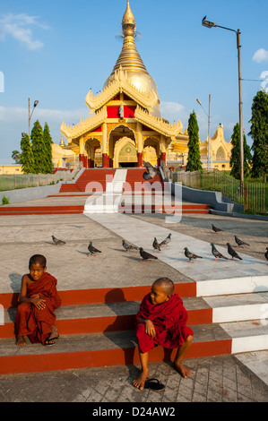 Zwei junge Novizin buddhistische Mönche sitzen auf Stufen außerhalb Maha Wizaya-Pagode in Yangon Stockfoto