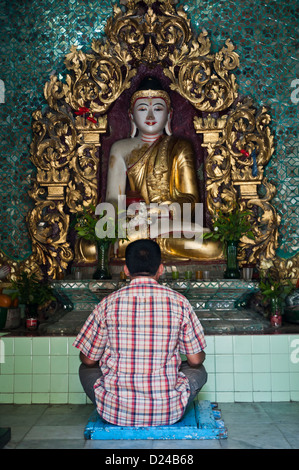 Ein Mann sitzt im Gebet vor einer Statue des Buddha bei Sule Pagode in Yangon, Birma Stockfoto