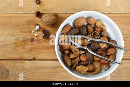 Nussmischung in einer weißen Schüssel mit einem Metall Nussknacker, fotografiert auf altem Holz Stockfoto