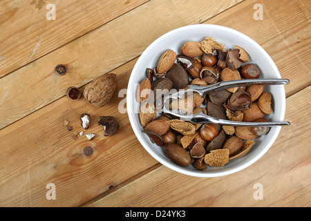 Nussmischung in einer weißen Schüssel mit einem Metall Nussknacker, fotografiert auf altem Holz Stockfoto