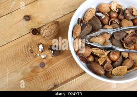 Nussmischung in einer weißen Schüssel mit einem Metall Nussknacker, fotografiert auf altem Holz Stockfoto